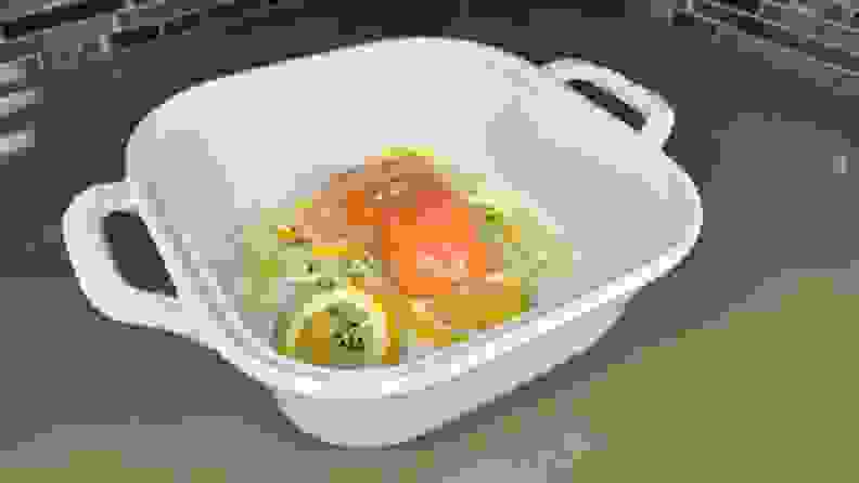 Thick piece of uncooked salmon with lemons inside of deep casserole dish.