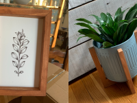 a black and white floral print inside a wooden frame, and at right, a plant grows inside a blue metal planter