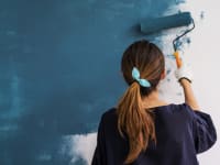 Woman painting a white wall blue with a paint roller
