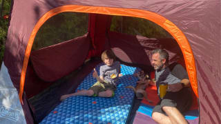 A child, a puppy, and a father recline in a Coleman Skylodge Instant Tent