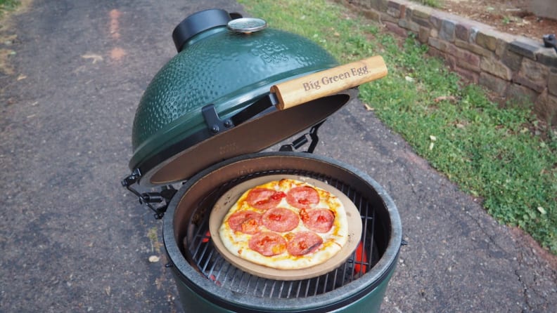 A Big Green Egg, opened, revealing a pepperoni pizza as it cooks.