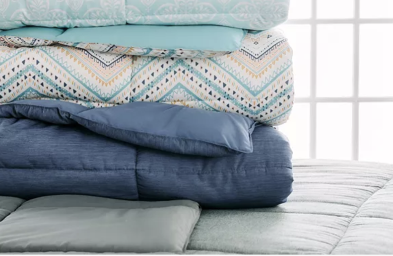 Four comforters in different shades of blue sitting on top of a bed.