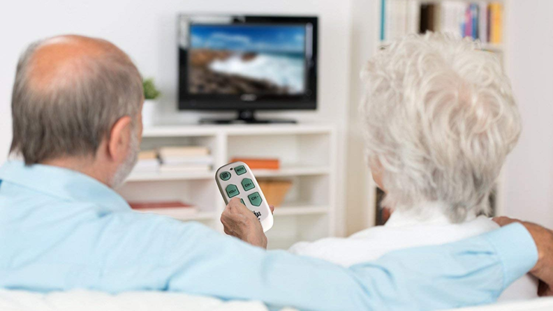 A senior couple navigate TV channels with a universal remote.