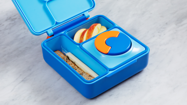 The OmiBox sits open on a marble counter with its Thermos in place and food in two compartments.