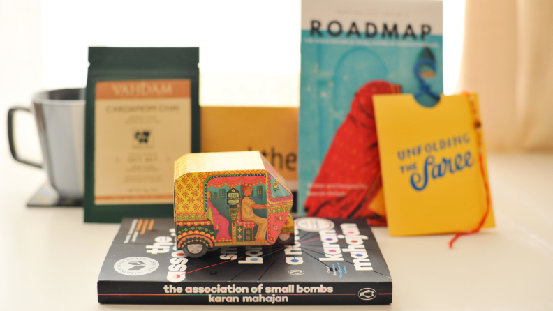 Small multi-colored cardboard electric tricycle sitting on top of novel, surrounded by tea cup and other books.
