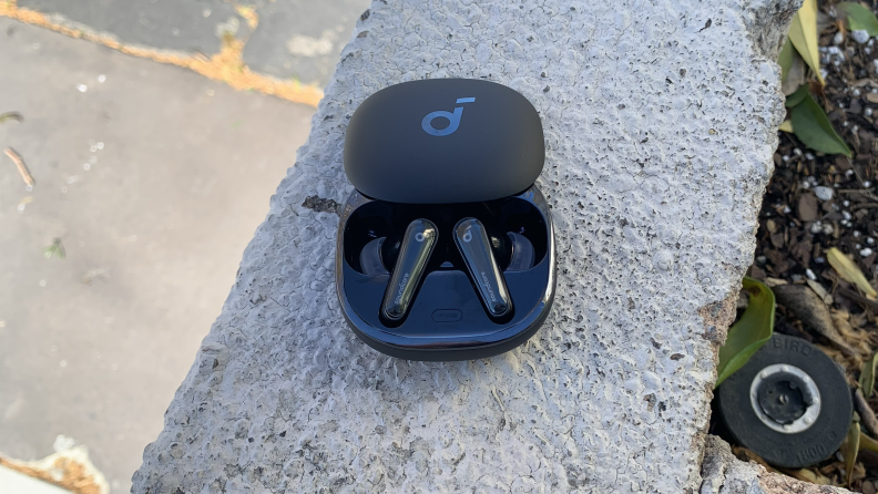The Anker Soundcore Liberty 4 in their open case that's sitting on a cement wall.