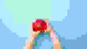一个蹒跚学步的孩子伸出双手，拿着一个淡蓝色背景下的红苹果。