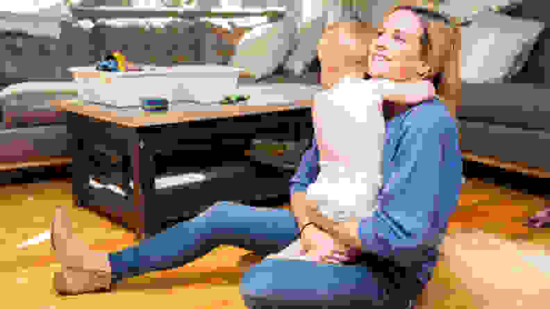 A mom sitting on the floor hugging a child wearing a pair of diapers