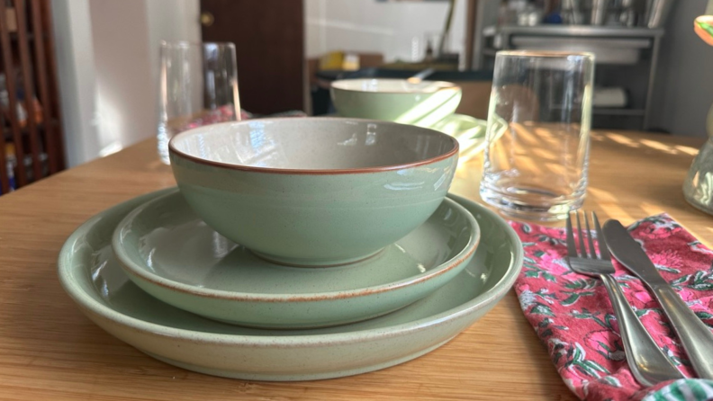 A stack of Denby dinnerware on a dinner table with glassware and silverware.