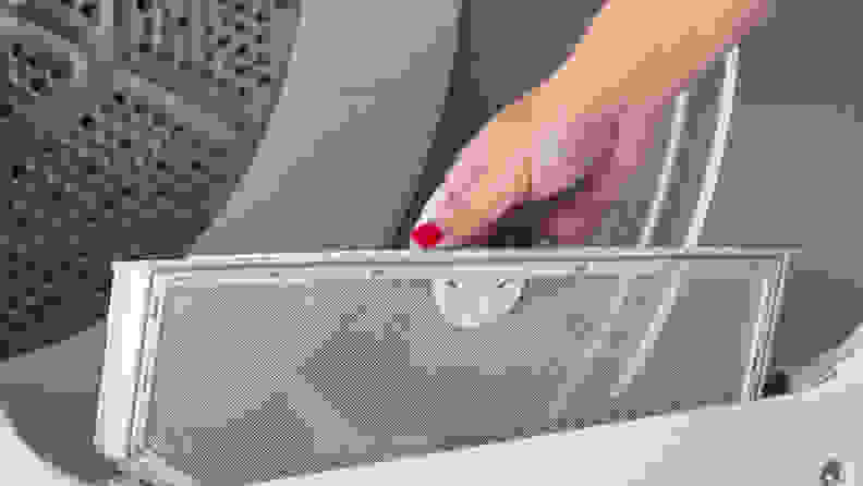 A hand reaches into frame, partially removing the GE GTD33EASKWW front-loading dryer's lint trap.