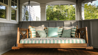 Wooden porch swing with pillows on sunny front porch.