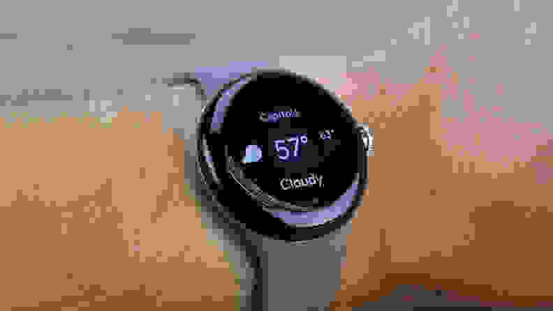 The Pixel Watch is shown on a wrist with a gray band and a circular black screen.