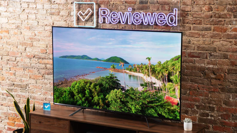 The Hisense U7H TV sitting on a wooden table in front of a brick wall.