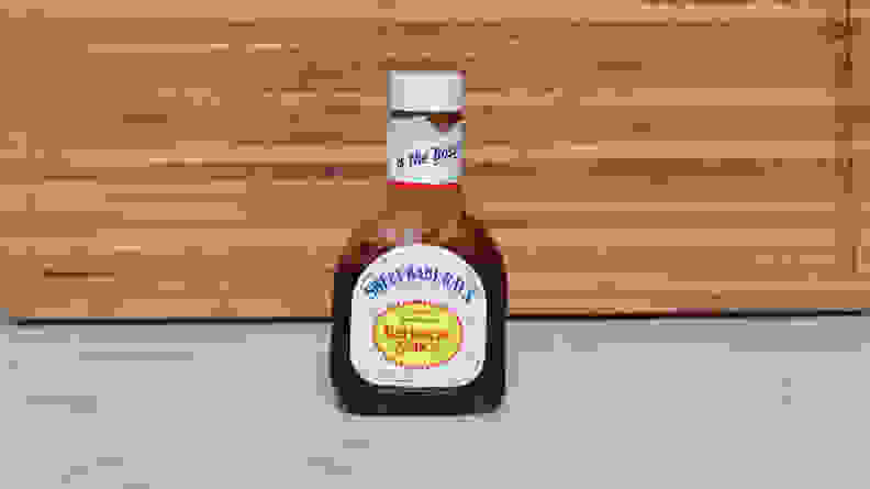 A bottle of  Sweet Baby Ray’s Barbecue  sauce next to a wood cutting board.