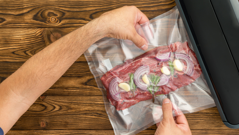 A person is vacuum sealing a bag of steak with herbs and spices using a food vacuum sealer.