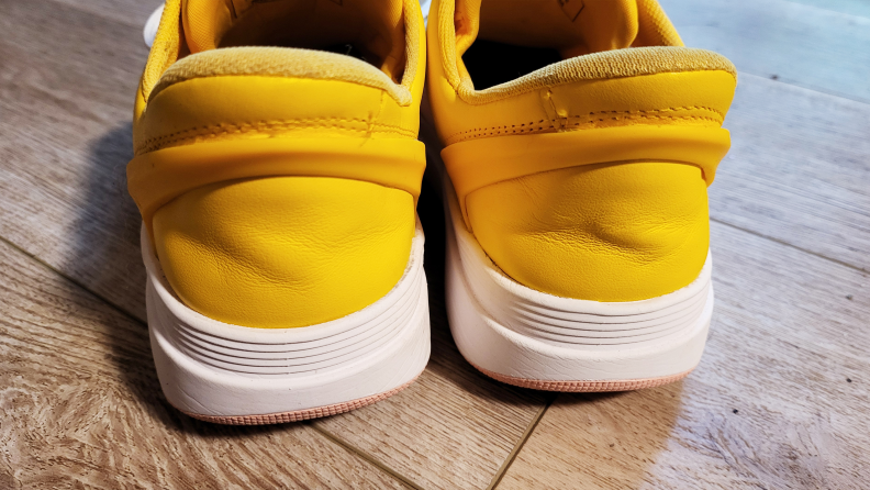 Backs of bright yellow and white Kizik Brisbane sneakers on woodgrain flooring