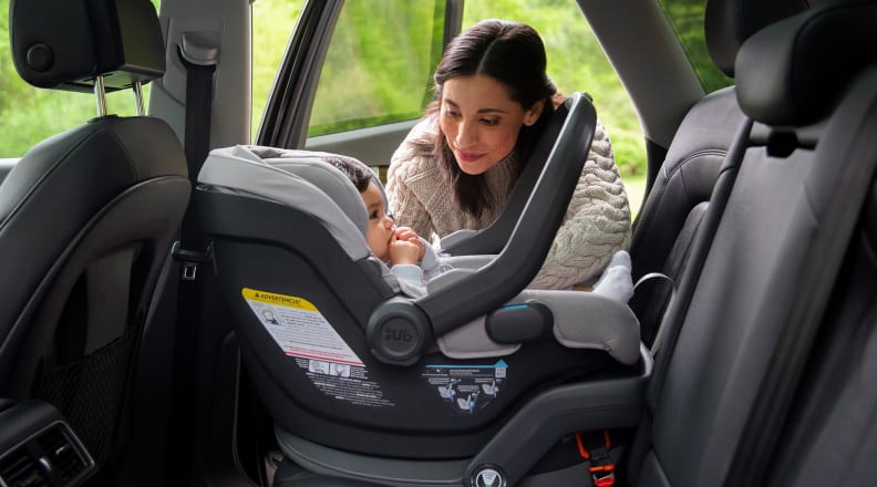 Person crouched near a baby in a car seat in the back of a cat