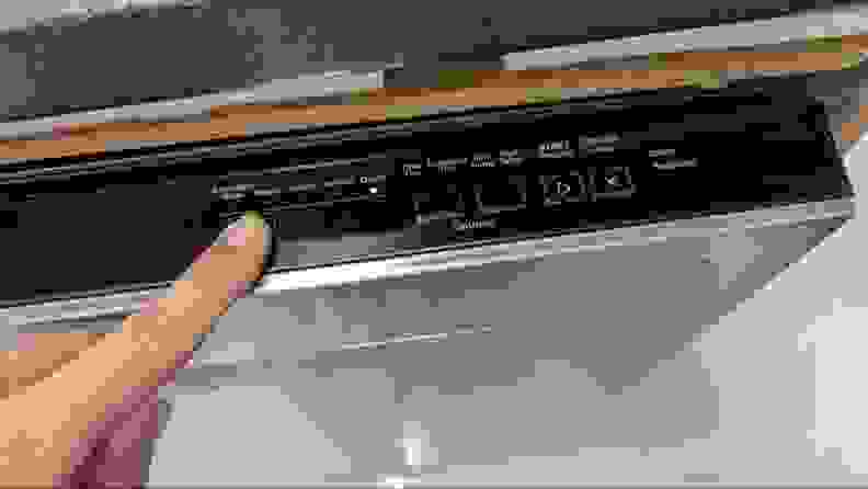 A finger reaches in from out of frame to point to the Whirlpool WDP540HAMZ's top-facing control panel.