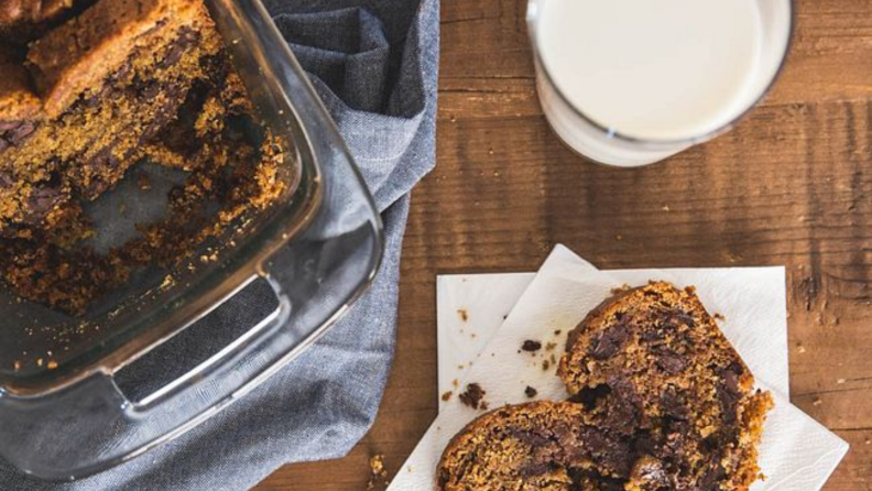 An image of a loaf pan with chocolate chip bread as seen from overhead, next to a slice of the same bread.