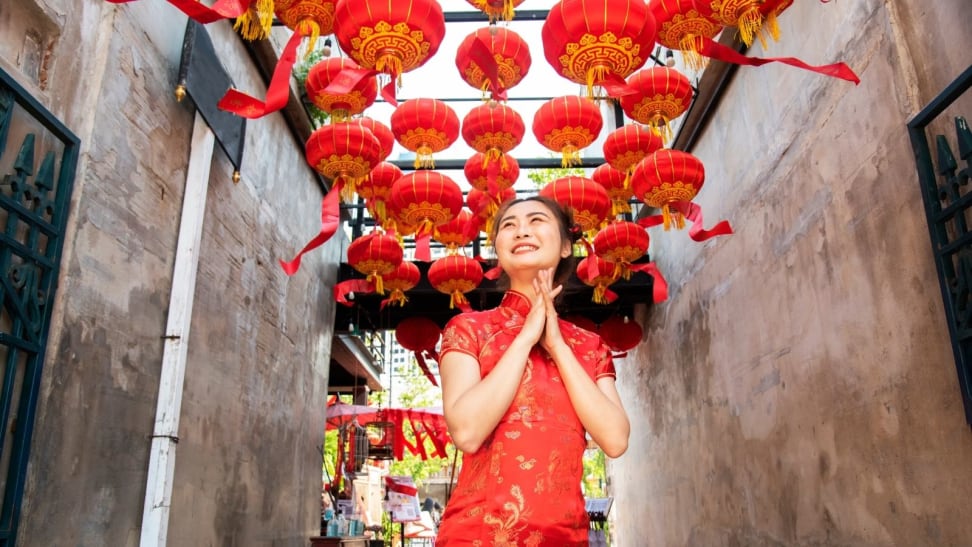 Woman standing underneath red lanterns, wearing traditional Chinese New Year attire.