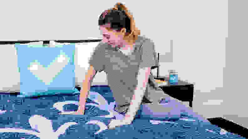 A person sitting on a mattress and pressing their hands into the surface.