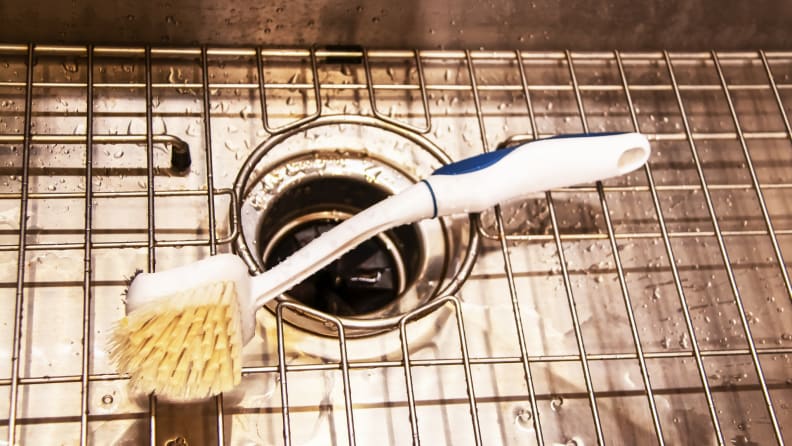 Long handle brush  sitting in kitchen sink on top of garbage disposal.