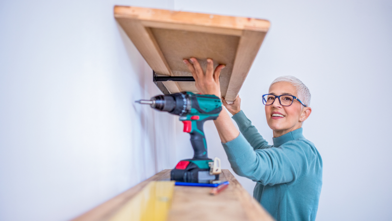 Person mounting wooden shelves on wall in home.