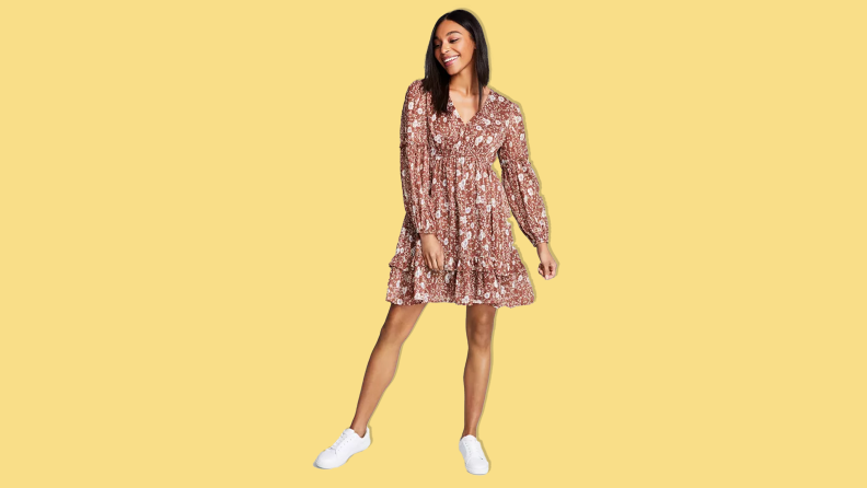 A woman wearing the And Now This Floral Fit and Flare Dress on a yellow background.