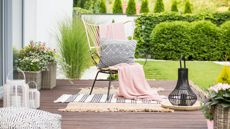 White pillow and pink blanket on a rattan chair standing in the garden of a luxurious house.