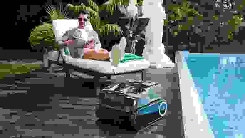 Man reads a magazine in a lounge chair to the left of the pool where the Aiper Scuba X1 Pro Max is