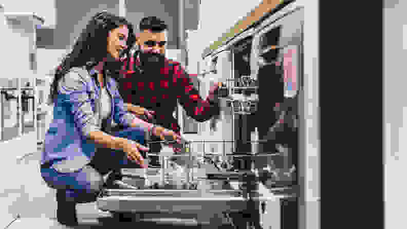 A man and woman delight over a dishwasher in a store.