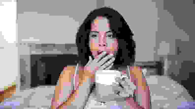 a person holds a cup of coffee lightly yawning