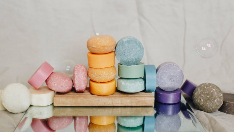 Shampoo bars in white, pink, orange, blue, purple, and gray stacked on top of each other in a line going across a table.