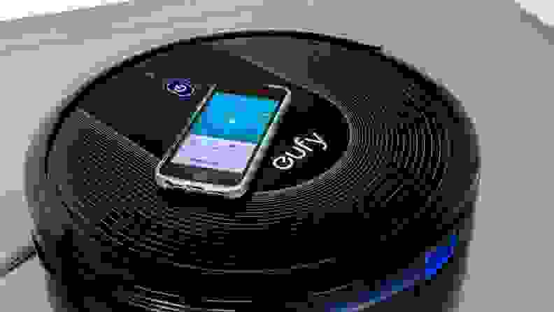Black robot vacuum by Eufy with smart phone resting on top