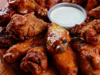 Wood plate of chicken wings running in stacked rings around a small plastic container of ranch dressing