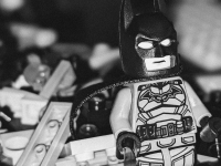 Close-up of a Batman Lego mini figure with a pile of gray and black Lego bricks in the background.