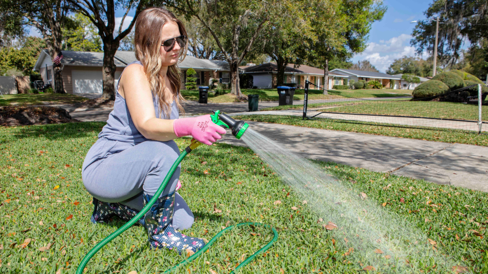 A person watering the grass with a garden hose