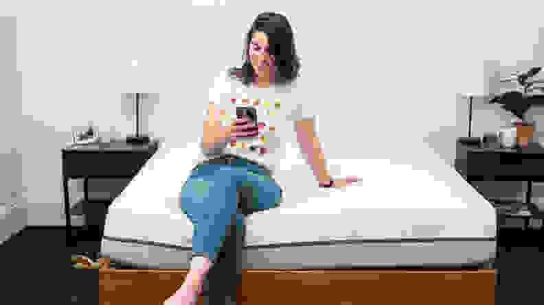 a person sits on the end of the Purple mattress on their phone