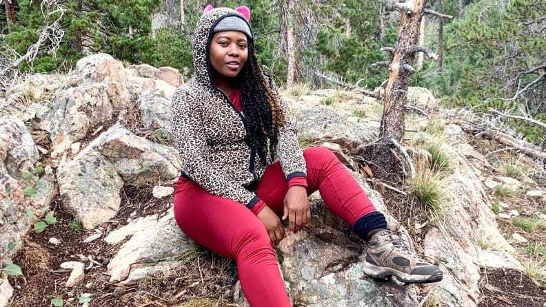A model poses outdoors wearing a knit hat, a leopard-print hoodie, and red thermal pants.