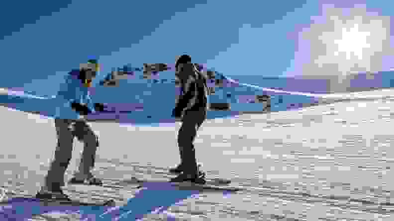 Two people skiing together on snowy mountainside.