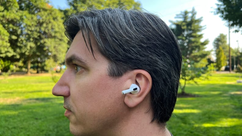 A man in a green park listens to a white AirPods Pro earbud.