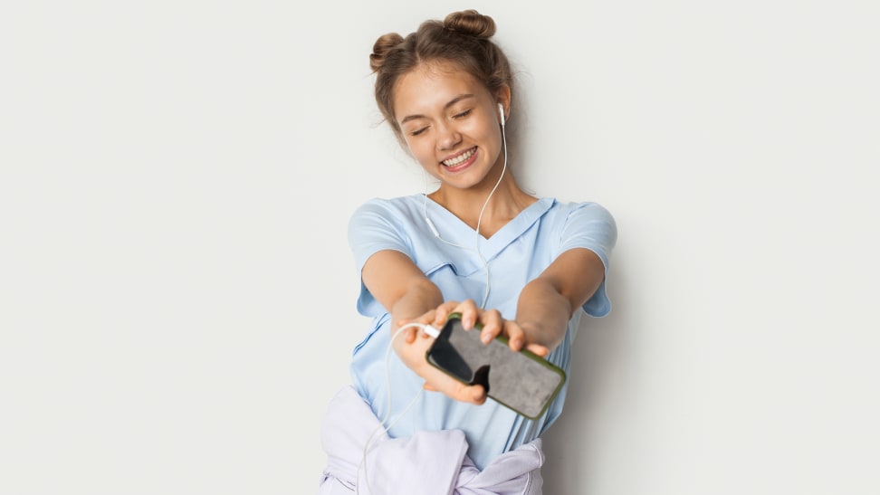 A young person smiles with arms outstretched while holding a smartphone.