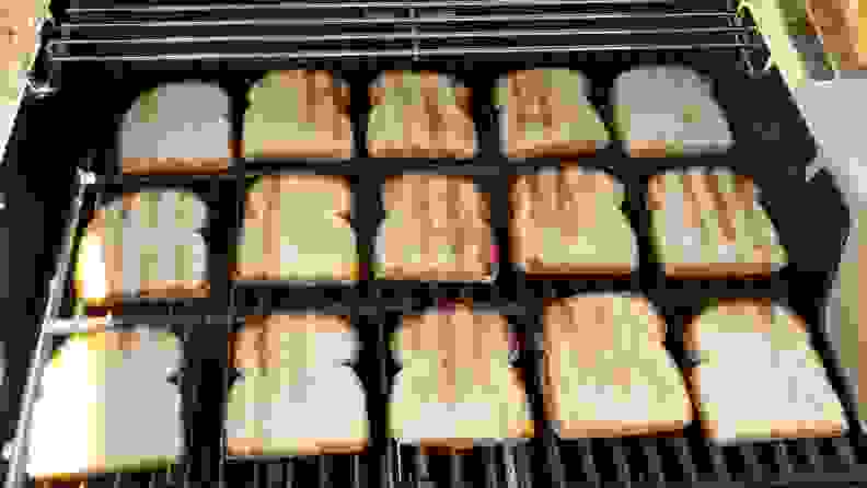 Grilled slices of white bread neatly arranged across the grate of a Weber grill.