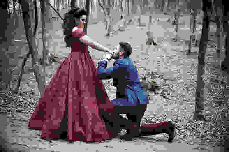Man on one knee proposing to woman in red dress