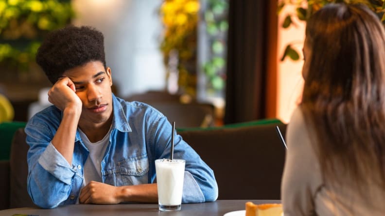 Person looking tired while leaning on hand at table with another person.