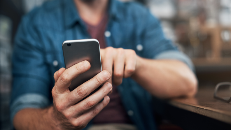 A man wearing a denim shirt dials a phone number on his cell phone