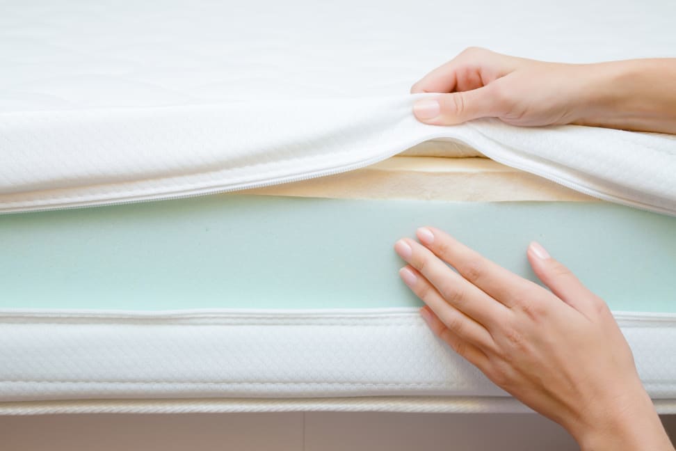 a woman's hand pulls up fabric covering to show foam inside a mattress