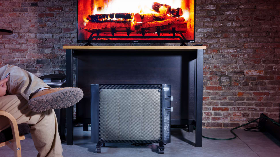 A space heater in a living room next to a person in a living room with a TV displaying an image of a fireplace