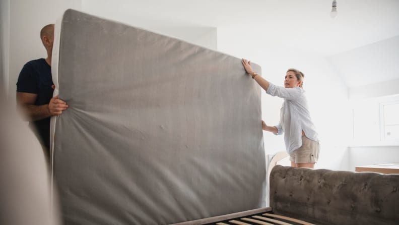 a man and woman move a mattress onto their bed frame
