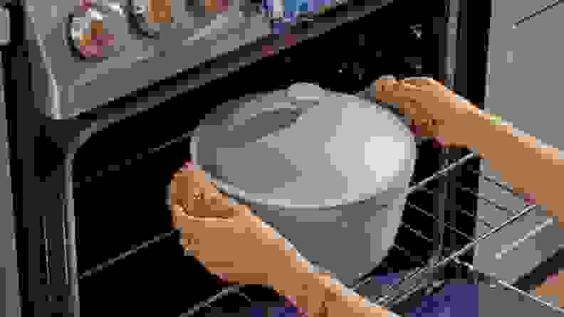 A person removes a pot that's covered with a lid from the oven.